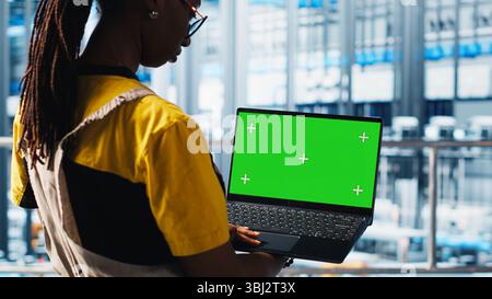 Smart factory specialist using mockup laptop to test automated systems and ensure reliability. Woman uses isolated screen notebook to identify bottlenecks and optimize equipment, camera A Stock Photo