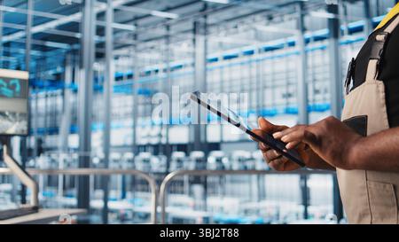 Smart factory expert using digital device app to test automated systems and ensure reliability. Worker uses tablet to identify bottlenecks and optimize gear based on sensors data, camera A close up Stock Photo