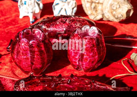 Jalon, Alicante - Spain - 12-14-2024: Two red glass decorative pieces with a textured pattern displayed on a red fabric-covered table, surrounded by v Stock Photo
