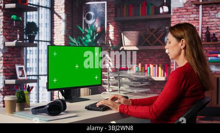 Confident woman solves freelancing tasks at copy space desktop, browsing the internet pages at her home office. Mature focused person self employed doing her job remotely. Camera B. Stock Photo