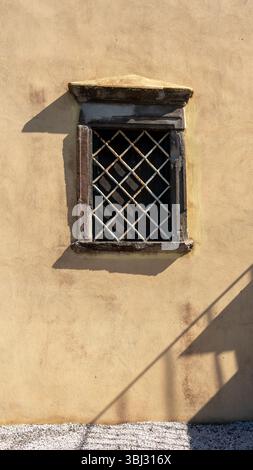 Old stone window with a security grille on a sunlit stucco wall Stock Photo
