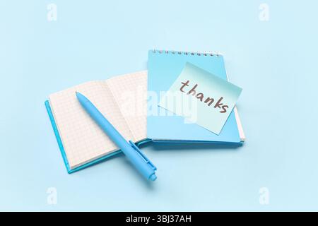 Sticky note with word THANKS, pen and notebooks on blue background Stock Photo