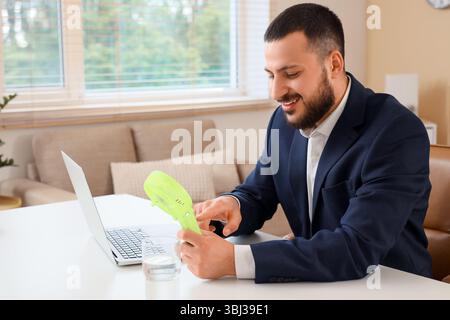 Young businessman turning on mini fan at table in office Stock Photo