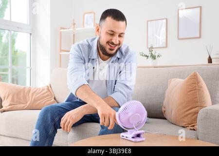 Young man turning mini fan on table at home Stock Photo