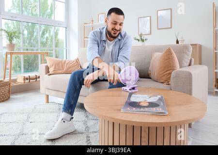 Young man turning mini fan on table at home Stock Photo