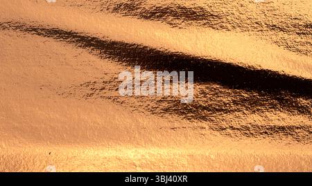 Copper metal plate with a shiny, grunge texture. Weathered, worn surface featuring a rusty, antique effect with a soft glow and fine metallic shine. L Stock Photo