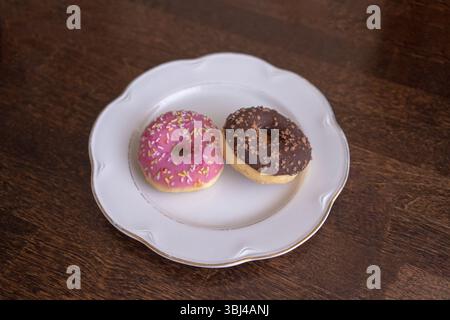 Donuts with chocolate and pink icing on a white plate on a wooden table Stock Photo
