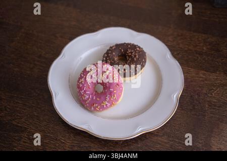 Donuts with chocolate and pink icing on a white plate on a wooden table Stock Photo