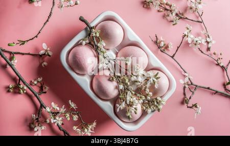 Pink Easter eggs in egg packaging on pale pink background with cherry blossom. Top view. Stock Photo