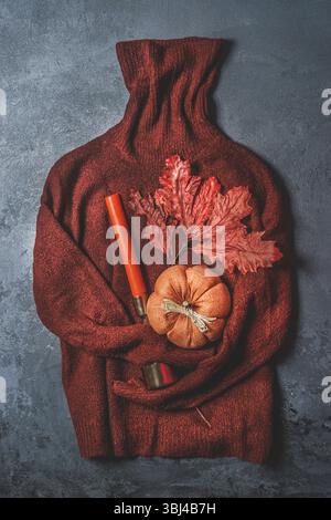 Brown knitted sweater with pumpkin, autumn leaf and orange candle on dark grey background. Seasonal autumn still life with warm clothes and fall decor Stock Photo