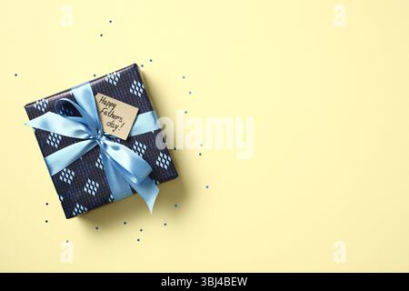 Happy Father's Day gift box with blue ribbon and tag on yellow background with confetti. Top view flat lay with copy space for text. Stock Photo