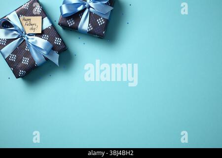 Father's Day gifts flat lay. Two blue gift boxes with ribbons and 'Happy Father's Day' tag on blue background with confetti. Top view, copy space. Stock Photo