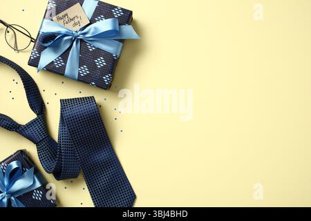 Father's Day flat lay with gifts, blue tie and glasses on yellow background. Stock Photo