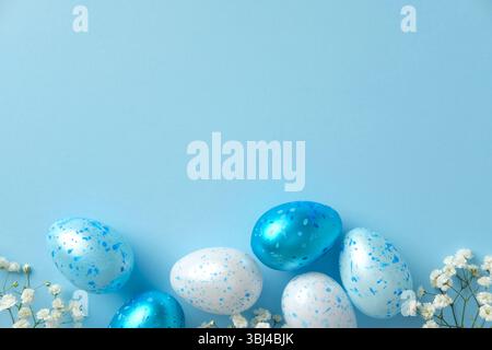 Blue and white speckled Easter eggs with white flowers on a pastel blue background. Flat lay, top view. Stock Photo