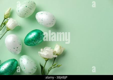 Green and white speckled Easter eggs with delicate white flowers on a pastel green background Stock Photo