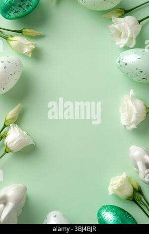 Easter flat lay composition with speckled eggs, white spring flowers, and pastel ceramic bunnies on a soft green background Stock Photo