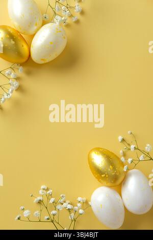 Golden and white Easter eggs with yellow speckles and delicate white flowers on a yellow background. Flat lay, top view, vertical Stock Photo