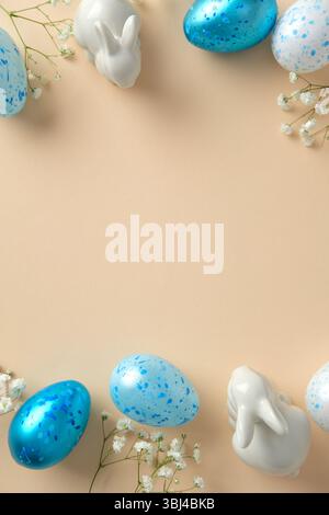Easter flat lay with blue speckled eggs, white ceramic bunny figurines, and delicate white flowers on a beige background Stock Photo