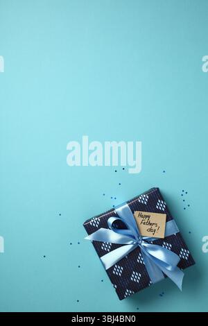 Father's Day gift box with blue ribbon and "Happy Father's day!" tag on a light blue background. Top view, flat lay concept for holiday celebration. Stock Photo