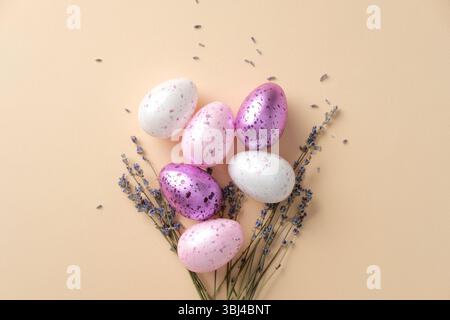 Stylish Easter composition with pastel speckled eggs, lavender sprigs, and a white ceramic bunny on a beige background. Flat lay, top view. Stock Photo