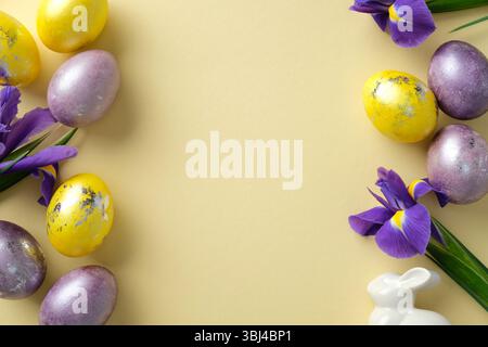 Easter flat lay composition with Easter eggs in purple and yellow shades with metallic details, and blooming purple irises on pastel yellow background Stock Photo