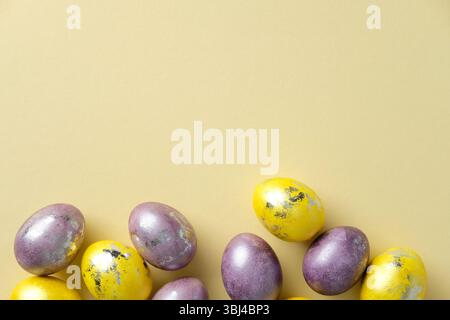 Vibrant Easter eggs in purple and yellow shades with metallic details on a pastel yellow backdrop. Flat lay, top view. Stock Photo