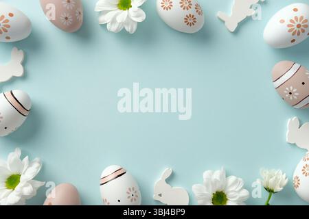 Easter frame. Flat lay composition with floral patterns Easter eggs, white daisies, and bunny cutouts on pastel blue background Stock Photo