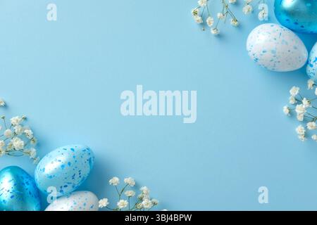 Pastel Easter scene with speckled blue and white eggs and small white flowers on a light blue background. Stock Photo