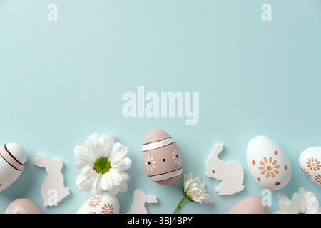 Decorated Easter eggs, daisies, and bunny silhouettes on a blue background. Flat lay, top view Stock Photo