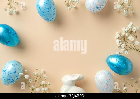 Easter flat lay composition with blue speckled eggs, white flowers, and a ceramic bunny on beige background Stock Photo