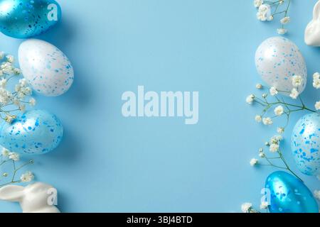 Blue and white speckled Easter eggs with delicate flowers and ceramic bunny on a pastel blue background Stock Photo