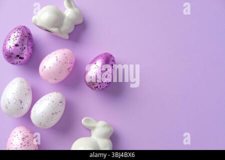Happy Easter concept. Flat lay composition with purple and white painted Easter eggs, ceramic bunnies on pastel purple background Stock Photo