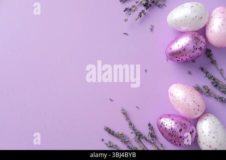 Happy Easter card design. Flat lay composition with pastel-colored speckled eggs and lavender flowers on a purple background Stock Photo
