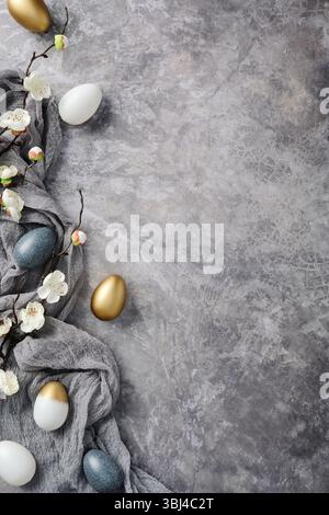 Easter flat lay featuring elegant golden and speckled eggs and blooming branches on textured gray background Stock Photo