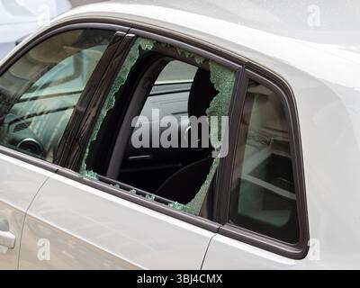 A close-up view of a car with a broken window, showcasing shattered glass pieces scattered around the interior. The cars interior is partially visible Stock Photo