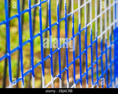 Close-up of a colorful fence with blue and gray grid patterns, showcasing the texture and structure of the mesh against a blurred natural background. Stock Photo