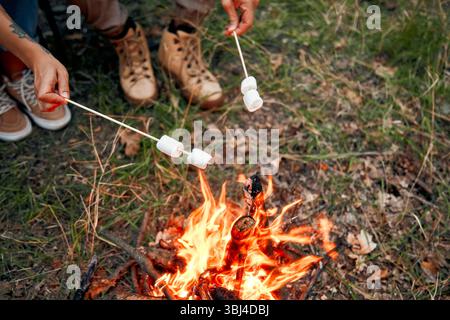 In a beautiful and serene outdoor setting, two people joyfully roast marshmallows over a cozy campfire, creating wonderful and lasting memories of fri Stock Photo