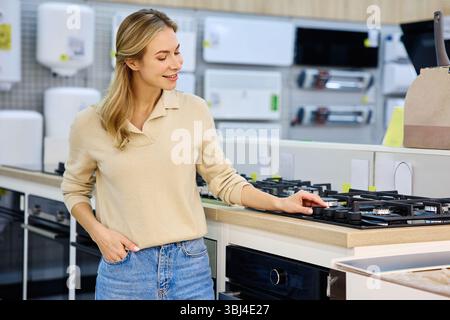 A young woman actively explores various kitchen appliances, showcasing her genuine interest in contemporary cookware and innovative home design elemen Stock Photo