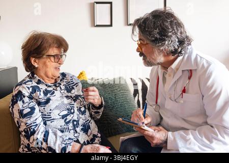Doctor visiting elderly woman at home taking notes of symptoms Stock Photo
