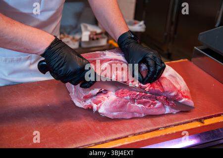 Butcher wearing black gloves skillfully cutting a vibrant piece of red meat with a sharp knife on a well used cutting board Stock Photo