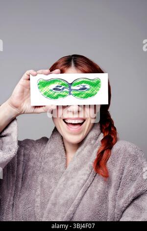 Happy woman wearing bathrobe holding green under eye patches smiling, promoting skincare and wellness Stock Photo