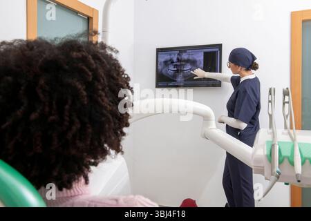 Dentist pointing at teeth x ray on digital screen, explaining diagnosis to patient in dental clinic Stock Photo