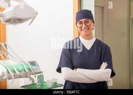 Confident female dentist smiling with crossed arms, showcasing professionalism and expertise in modern dental clinic Stock Photo