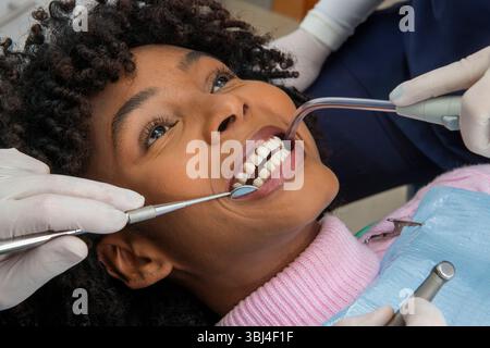 Dentists performing a check up on a smiling female patient, using specialized tools for cleaning and examining her teeth Stock Photo