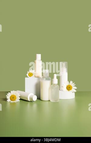 White cosmetic bottles with chamomile daisy flowers green background Stock Photo