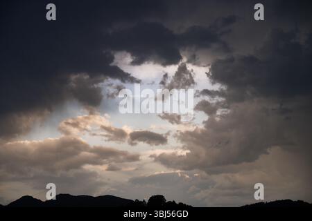 Dark clouds covering the sky letting only a few rays of sunlight pass through, creating a dramatic scene over the mountains Stock Photo
