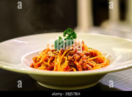 Close up beautiful spaghetti bolognese in the dark environment of a restaurant. Side view image of spaghetti bolognese in white dish. Stock Photo