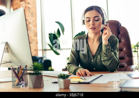 Professional businesswoman wearing headset working at desk, focused on tasks in a modern office environment Stock Photo