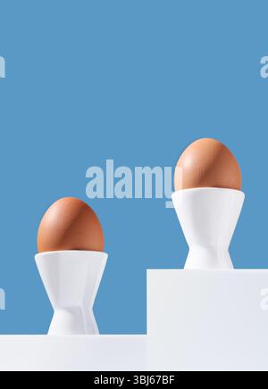 Two brown chicken eggs stand in egg-cups on white catwalks on a blue background. Copy space. Stock Photo
