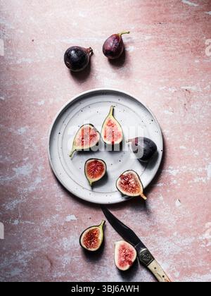 Fresh figs whole and cut displayed on plate with knife on pink surface.jpg Stock Photo